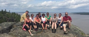 A group on top of Devil's Rock with a spectacular background view of lake Temiskaming. Perfect outing during your stay at the Presidents' Suites in Haileybury. / Un groupe au rocher du diable avec une vue spectaculaire du lac Témiskaming. Expédition parfaite pendant votre séjour aux Suites des Présidents à Temiskaming Shores.